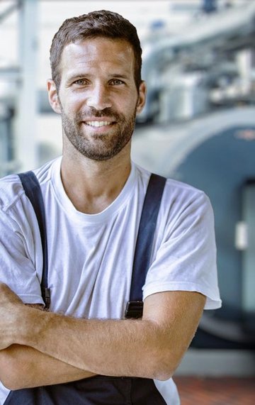 Ein Mann in Arbeitskleidung mit verschraenkten Armen