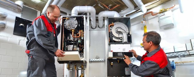 Zwei Techniker arbeiten in einem Heizungsraum, einer hält ein Gerät, während der andere Einstellungen vornimmt.