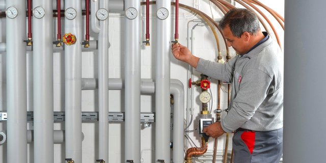 Ein Techniker überprüft die Druckanzeigen an einer Reihe von Rohren in einem modernen Heizungsraum.