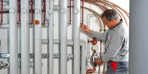 Ein Techniker überprüft die Druckanzeigen an den Rohren in einem modernen Heizungsraum, konzentriert und professionell.