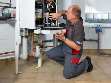 Ein Techniker kniet vor einer Heizungsanlage und arbeitet an der Elektronik, um eine Reparatur durchzuführen.