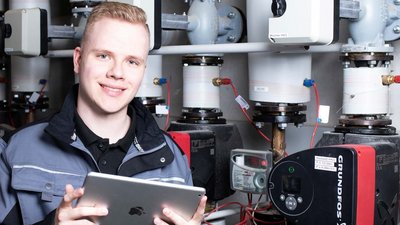 Ein junger Anlagenmechaniker vor einer Heizungsanlage, der ein Tablet hält 